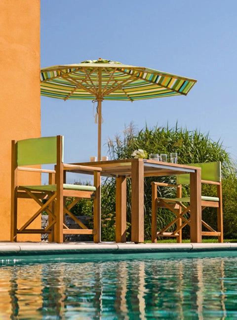 Wetterfeste Regiestühle Cabin aus Teakholz mit dem Stoff Apfelgrün als Sitzgruppe um einen Tisch neben einem Pool.