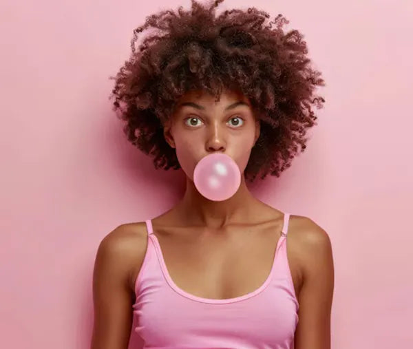 Frau mit Kaugummiblase vor rosa Hintergrund als Verdeutlichung für das neue Aussehen von Regiestuhl.