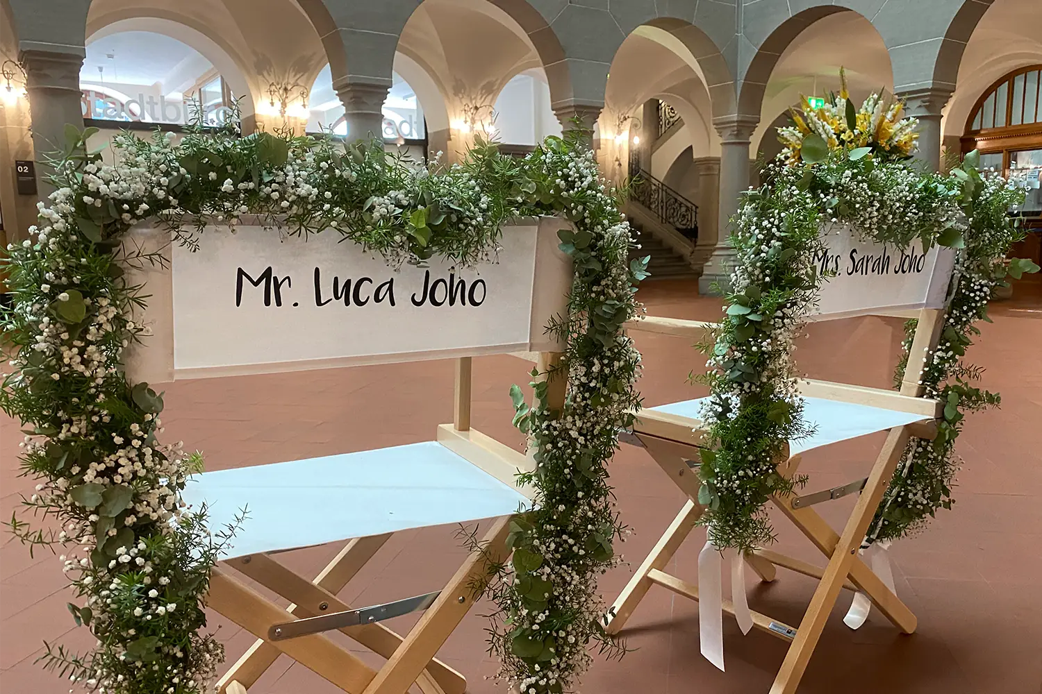 Zwei personalisierte Regiestühle Alfred mit Namen, behängt mit Blumenschmuck als stilvolle Sitzgelegenheit für das Brautpaar im Standesamt oder bei der Hochzeitsfeier
