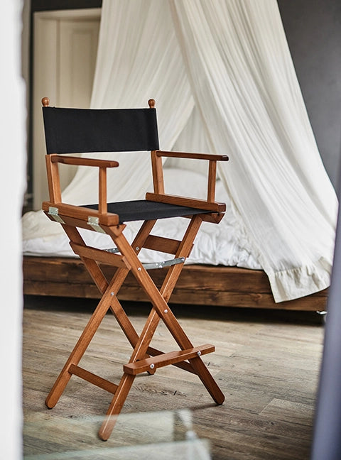 Hoher Regiestuhl Steven in braunem Holz und mit schwarzem Stoff steht in einem Schlafzimmer.