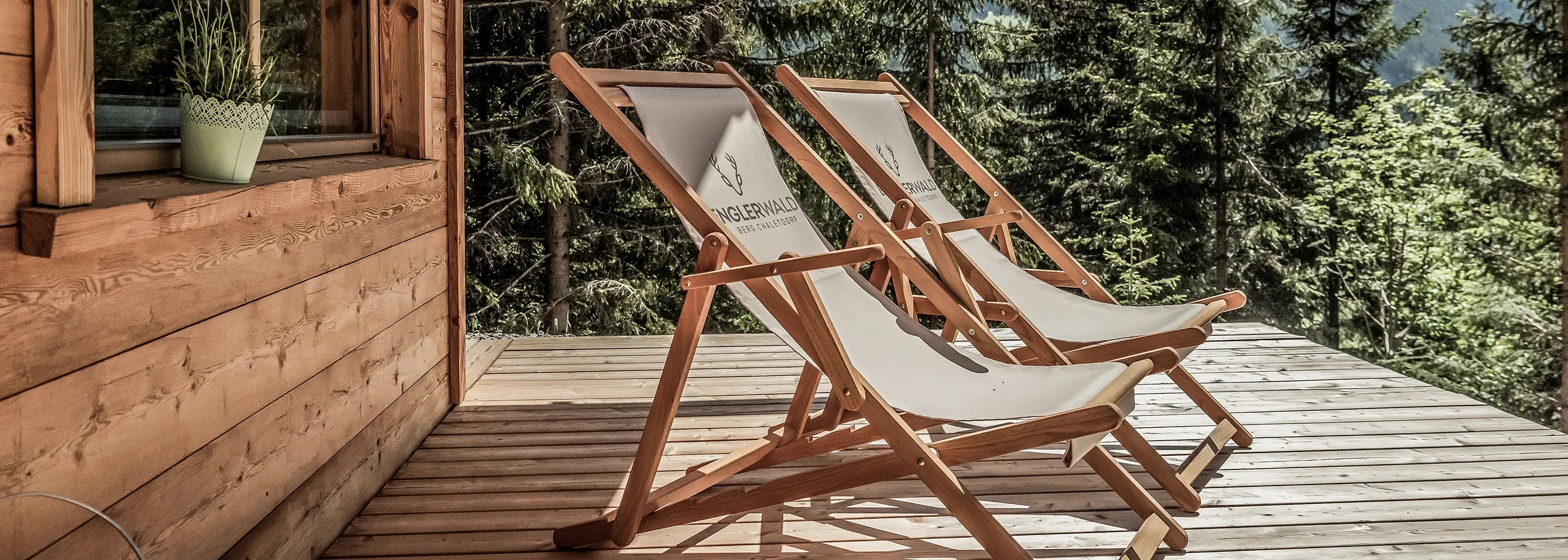 Zwei Liegestühle Charly mit Logo auf einer Hotelterrasse vor Alpenpanorama.