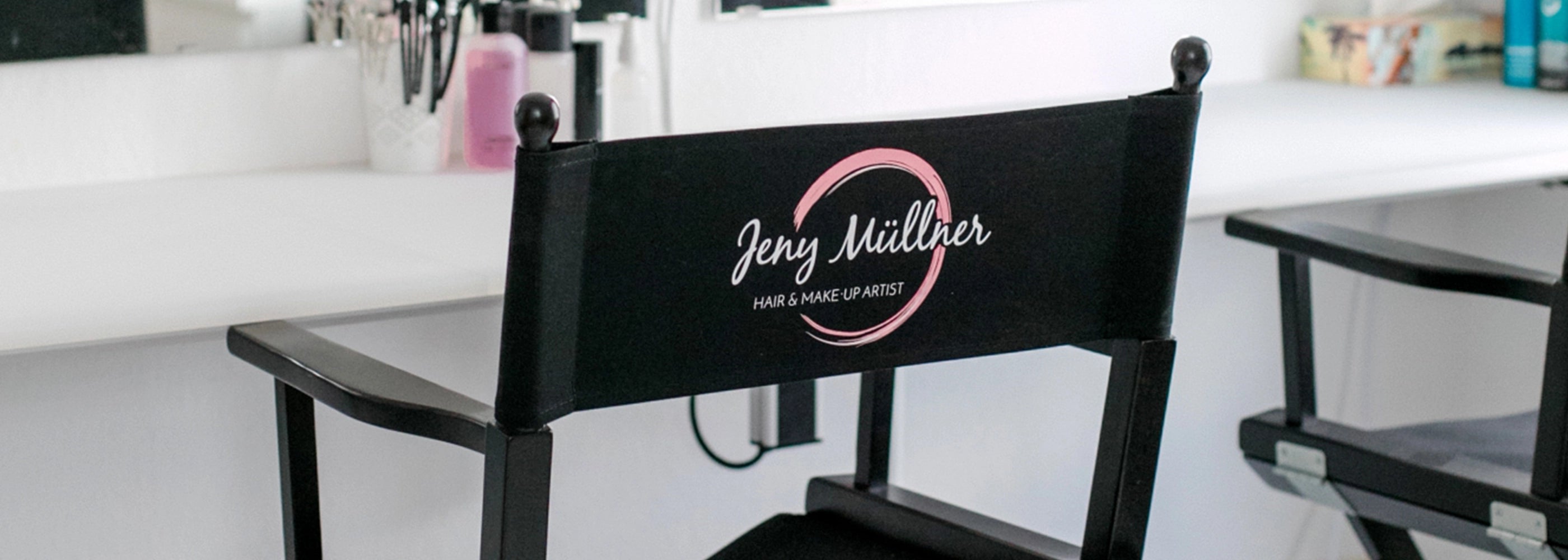 Schwarzer Make-Up-Stuhl mit Logo-Bedruckung vor beleuchtetem Spiegel im Kosmetikstudio