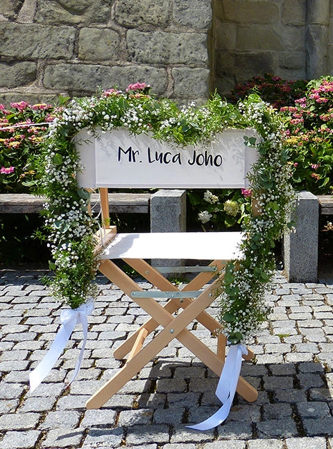 Personalisierter Regiestuhl Alfred in natur mit weißem Bezug, Namensaufdruck und floralem Herzkranz für eine stilvolle Hochzeitsdeko