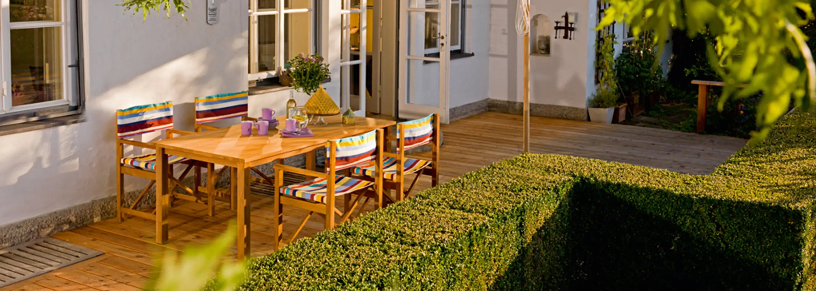 Holzregiestühle Cabin mit gestreiftem Bezug auf einer sonnigen Holzterrasse im Garten.