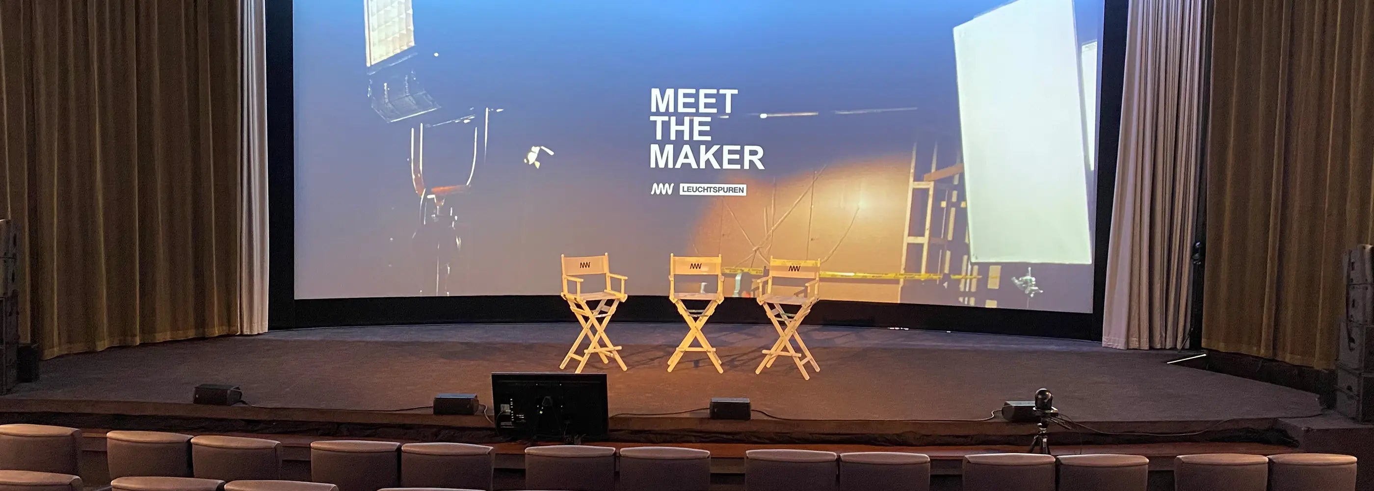 Drei weiße Regiestühle Steven mit Logo auf einer Kinobühne vor einer Großleinwand – perfekte Ausstattung für Panels, Premieren oder Talks.