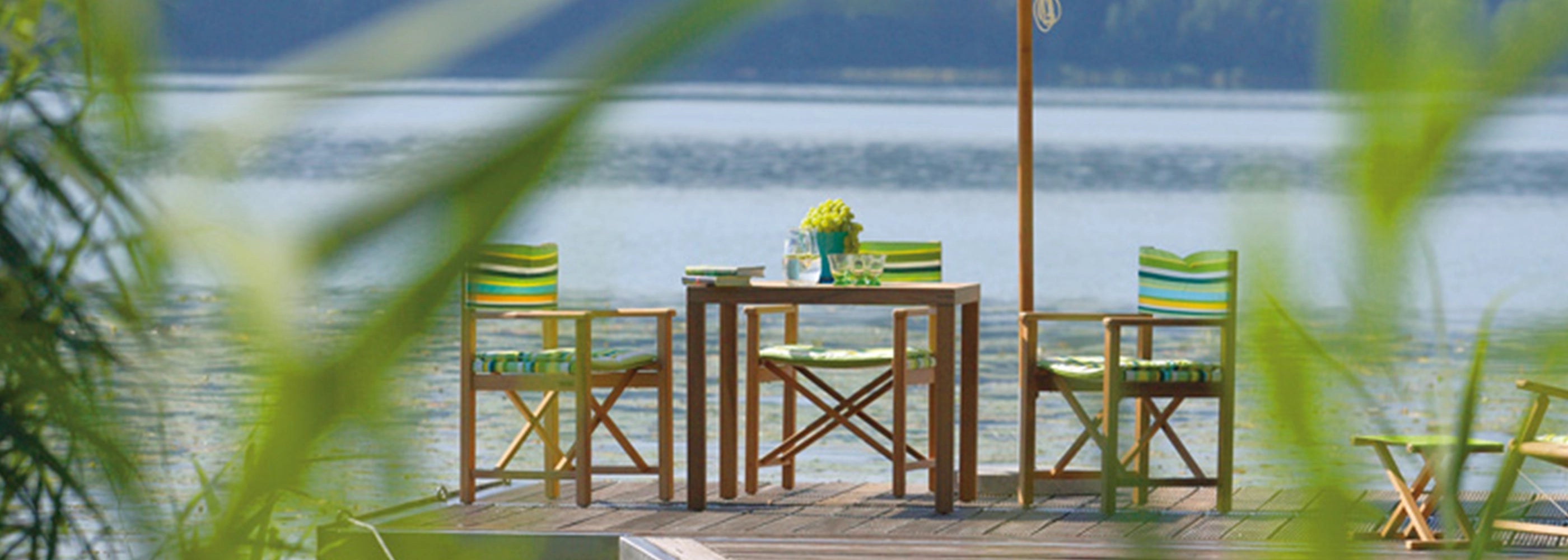 Wetterfeste Regiestühle Cabin aus Teak Holz auf einem Steg am See mit Sonnenschirm.