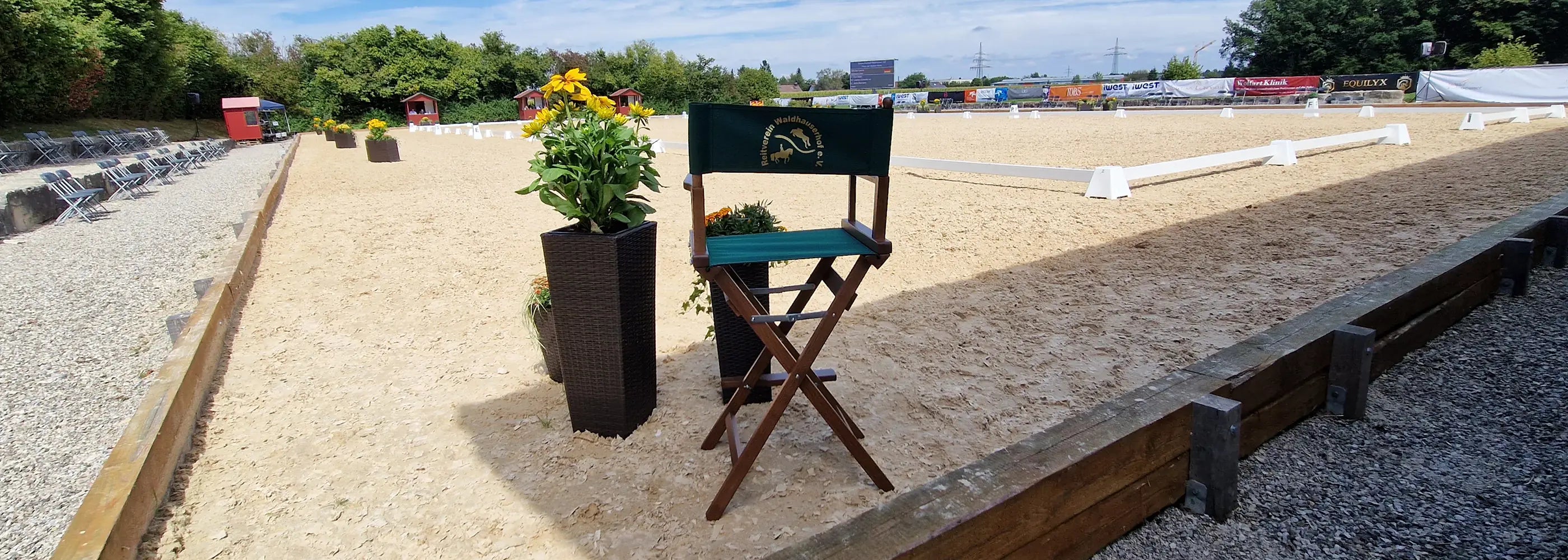 Regiestuhl mit Vereinslogo am Reitplatz bei Turnierveranstaltung, Tribüne im Hintergrund.