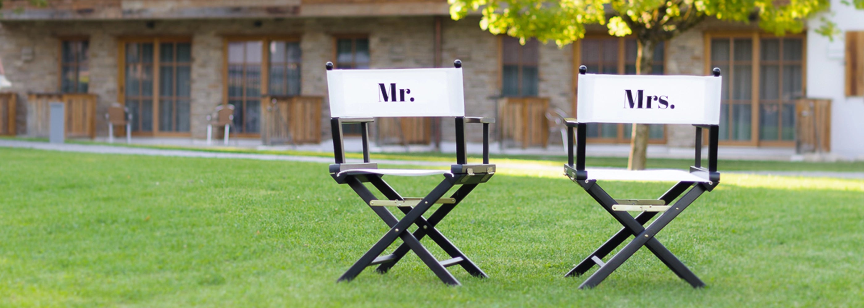 Zwei Regiestühle Alfred mit schwarz-weißem Design und „Mr.“ & „Mrs.“ Schriftzug im Grünen – ideal für Hochzeiten & als Geschenk.
