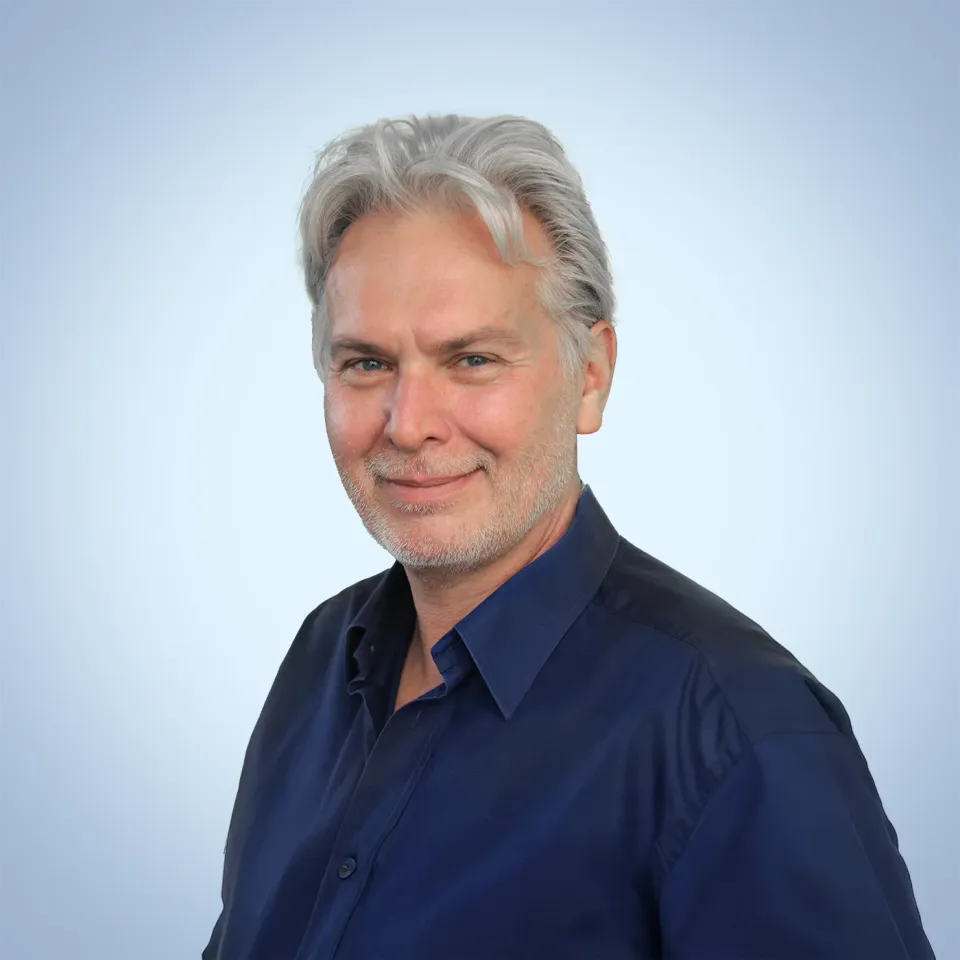 Günther vom Regiestuhl-Team in dunkelblauem Hemd vor hellblauem Hintergrund