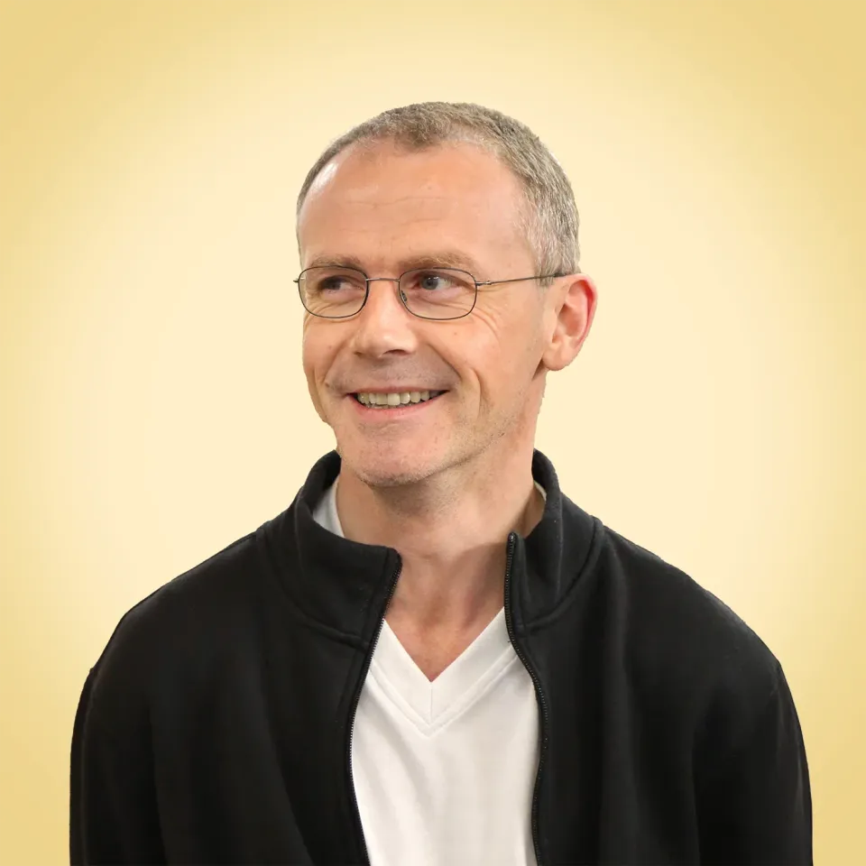 Brian vom Regiestuhl-Team mit Brille und sportlichem Look vor gelbem Hintergrund