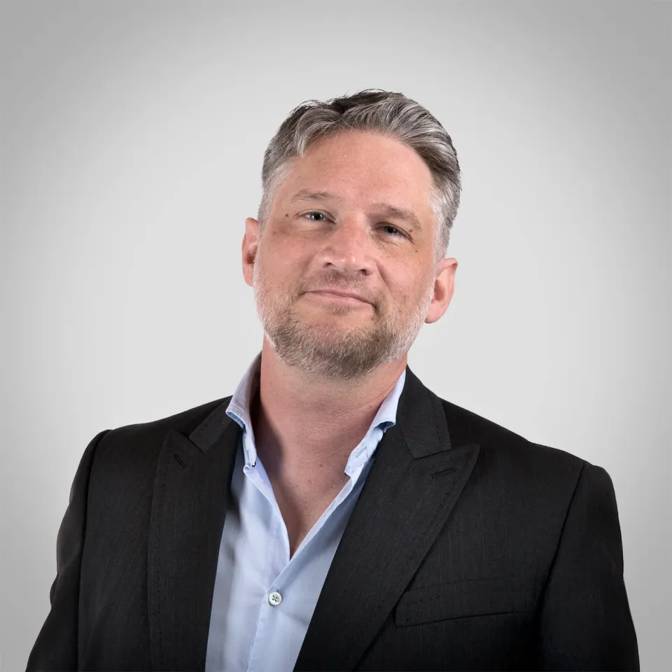 Johannes vom Regiestuhl-Team mit grauen Haaren und charismatischem Blick vor hellgrauen Hintergrund