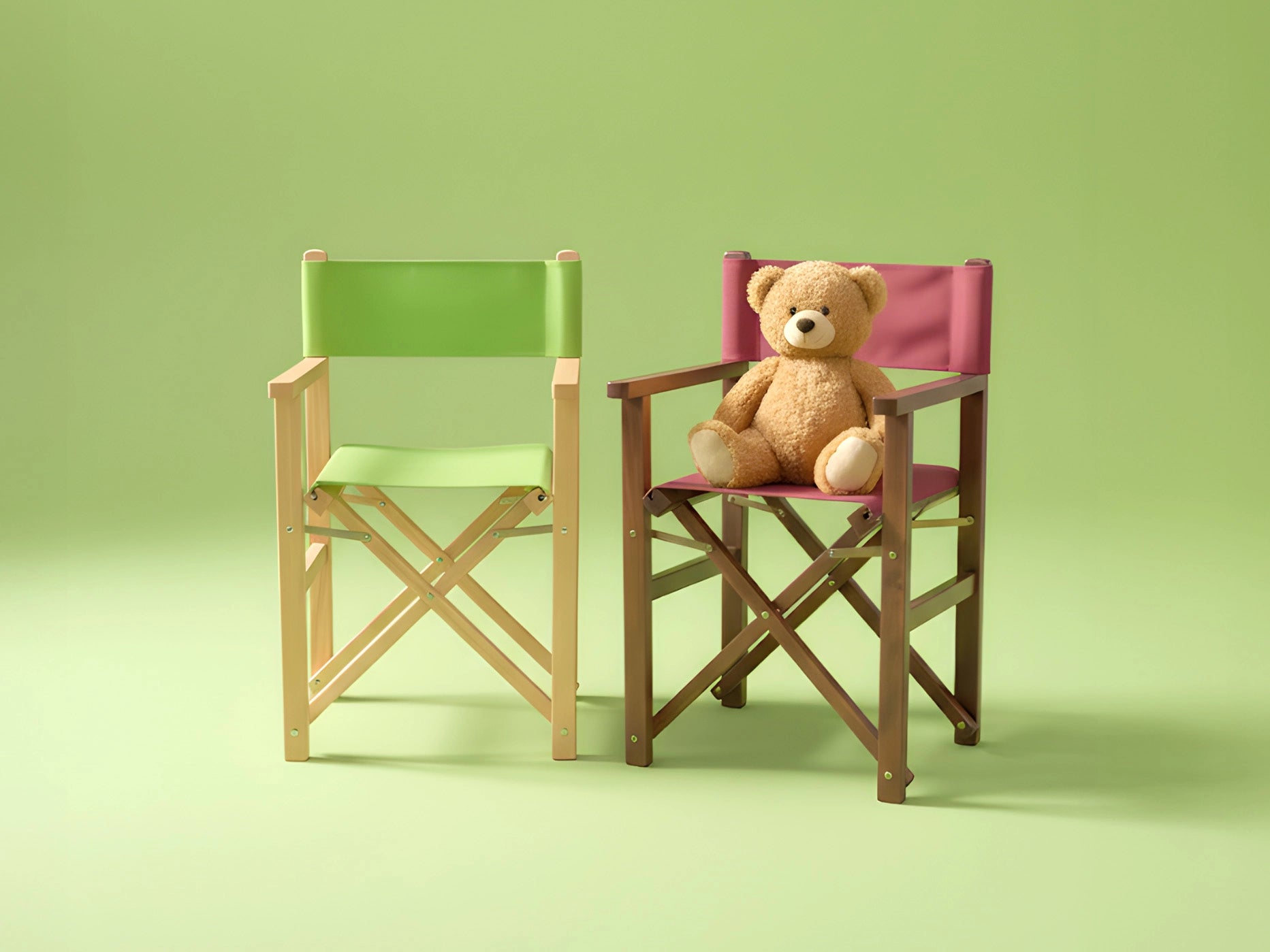 Zwei farbige Kinder-Regiestühle, einer mit Teddybär, vor grünem Hintergrund