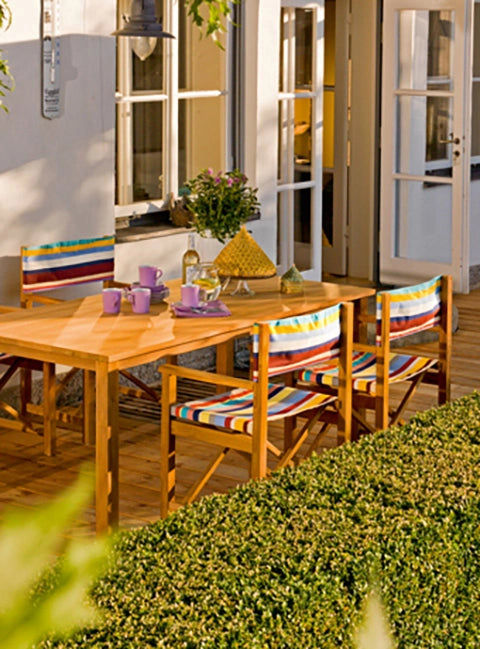 Wetterfeste Regiestühle Cabin aus Teakholz mit dem Stoff Multicolor als Sitzgruppe um einen Tisch auf einer Terrasse.