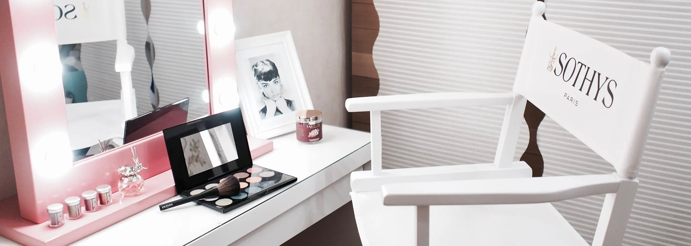 Weißer Make-Up-Stuhl mit Logo-Aufdruck vor beleuchtetem Spiegel in elegantem Stylingraum