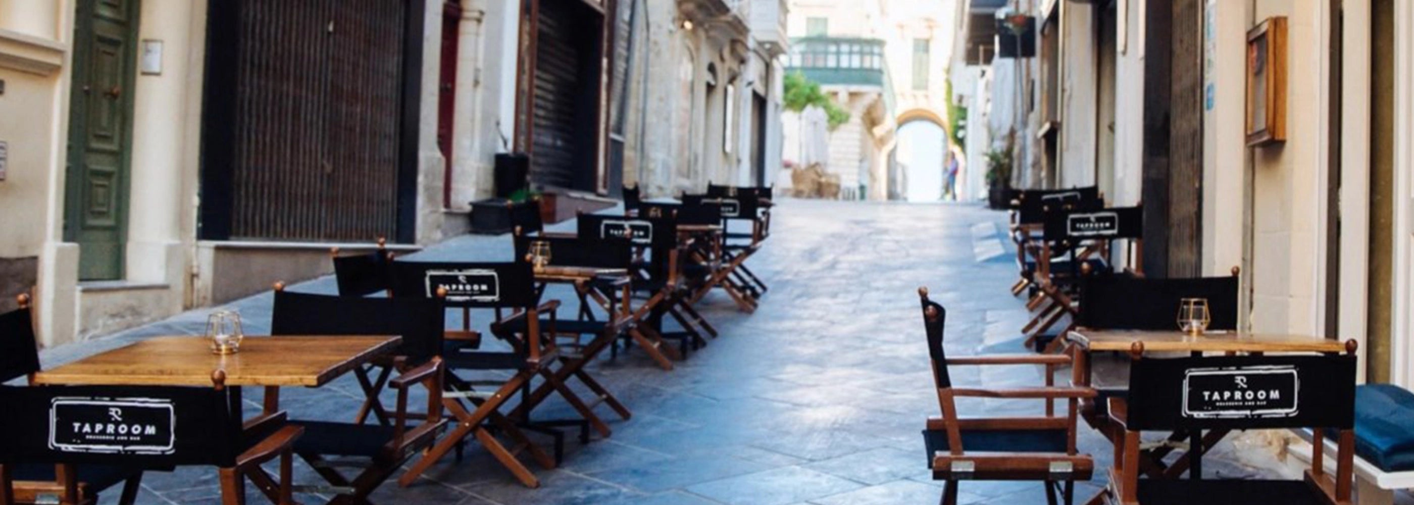 Holzregiestühle mit schwarzem Stoff und Logodruck in mediterraner Altstadtgasse