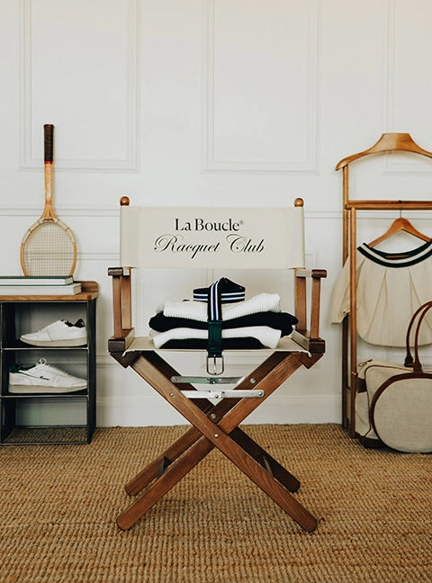 Regiestuhl Alfred mit Logo bedruckt – eleganter Holzstuhl in braunem Holz mit naturfarbenem Bezug in einer Retro-Tennis Umgebung.