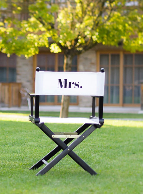 Personalisierter Regiestuhl Alfred mit schwarzem Gestell und weißem Bezug mit Druck "Mrs." auf Rückseite. Stilvolle Sitzgelegenheit für Hochzeiten, Fotospots und Events.