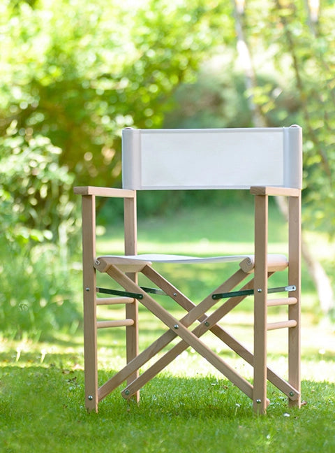 Regiestuhl Billy aus naturbelassenem Holz mit weißem Stoff steht in einem grün-blühenden Garten.