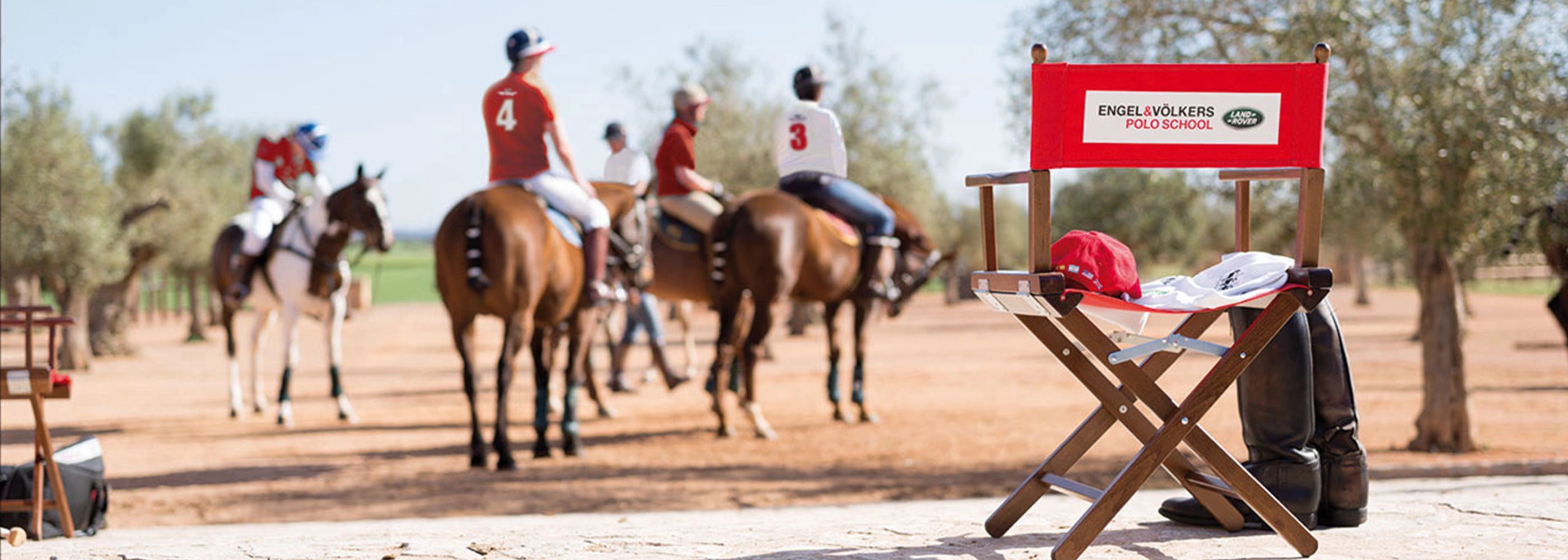 Regiestuhl Alfred mit rivarotem Stoff und Logo-Bedruckung am Rande eines Polofelds – bereit für den Einsatz bei Sportevents oder Outdoor-Veranstaltungen.