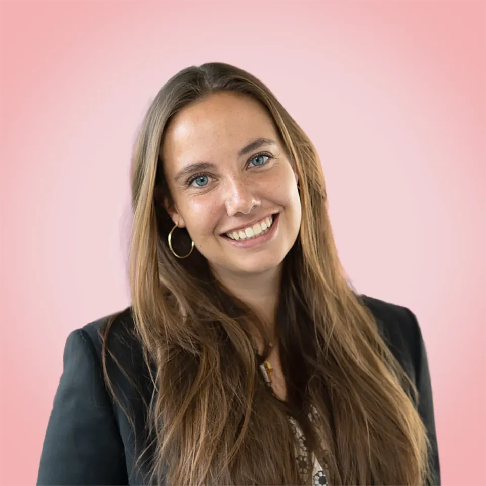 Alina vom Regiestuhl-Team mit langen Haaren und freundlichem Lächeln vor rosafarbenem Hintergrund