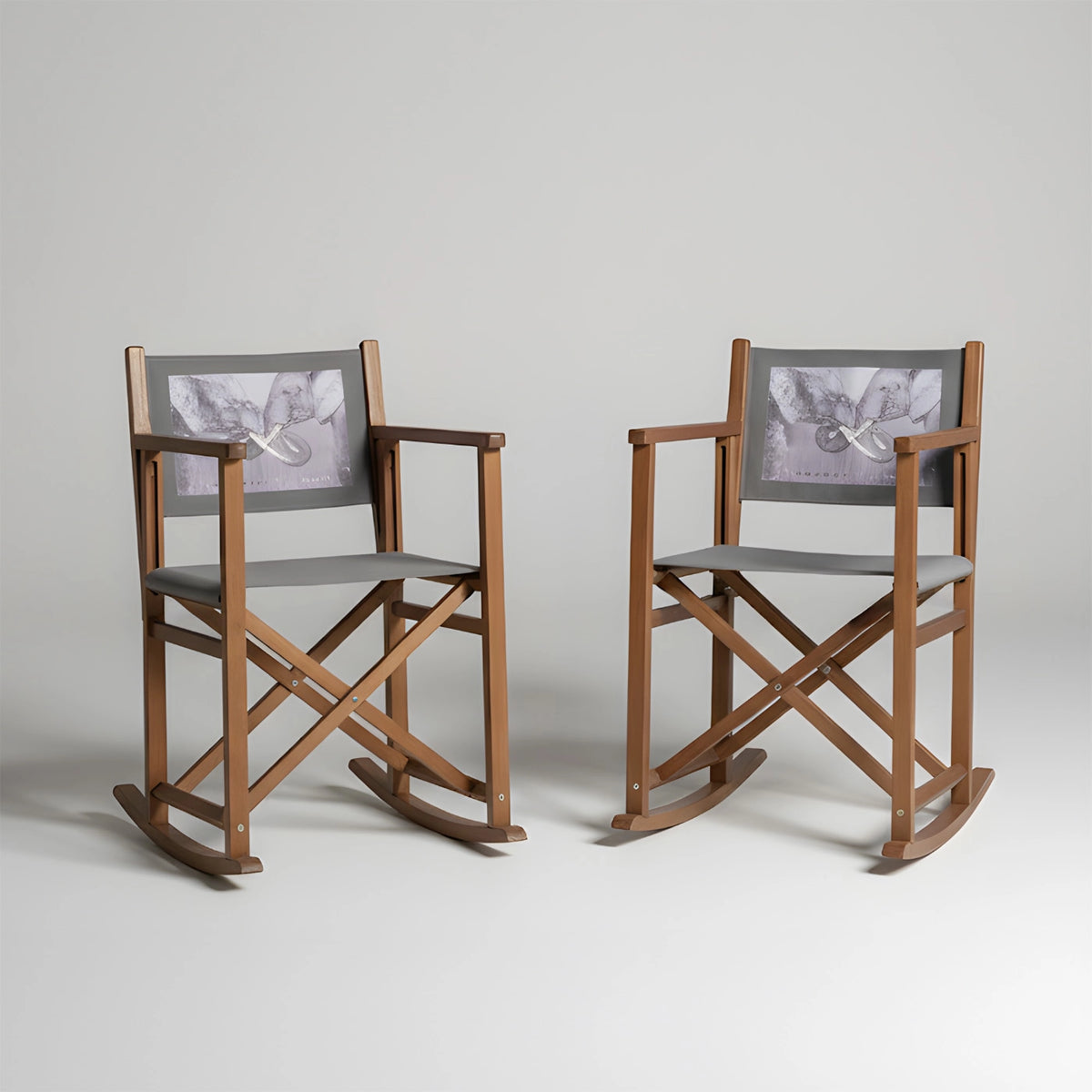 Zwei Schaukel-Regiestühle mit grauen Stoffen und individuellem Druck vor neutralem Hintergrund (quadratisch)